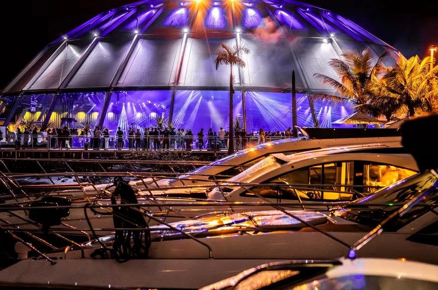 Lanchas atracadas em frente à tenda iluminada do LAROC à noite